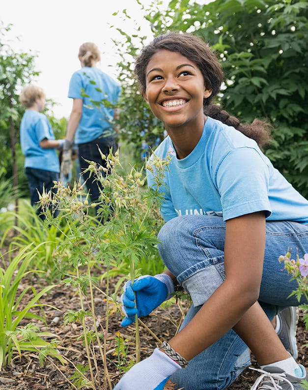 A woman in jeans and gardening gloves crouched down in a garden space