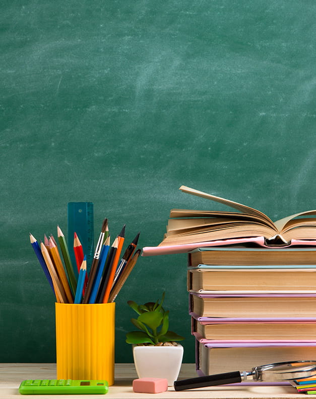 A stack of books standing in front of a chalk blackboard. There is a pot of pencils sitting to the side of the books