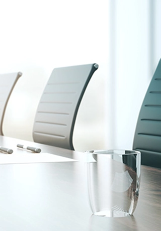 A long row of executive chairs at a board table. There are glasses of water at the table and a piece of white paper at each seat. The image fades from the right to the left
