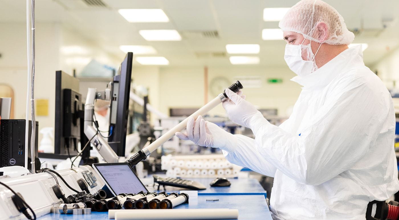 A Watson-Marlow Fluid Technology Solutions colleague wearing a white suit, hairnet and mask working in a clean environment