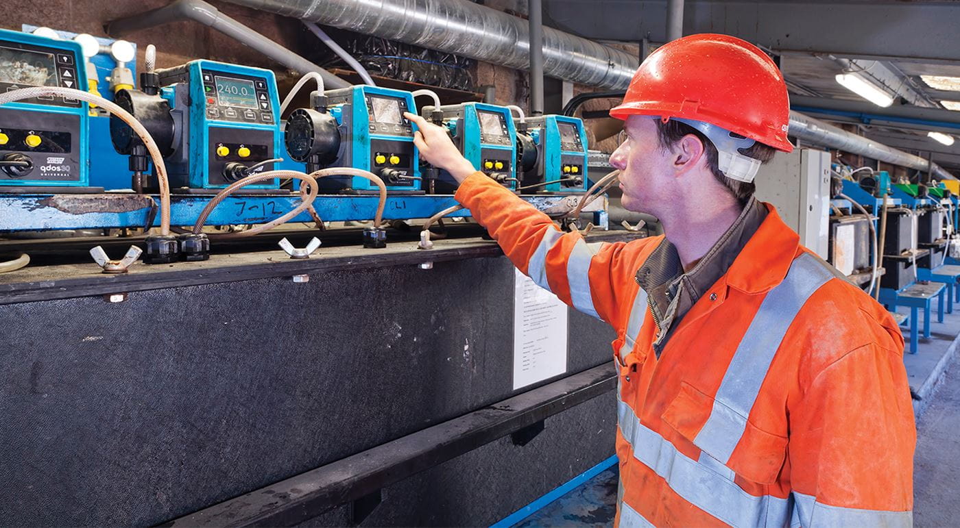 A male colleague in a hi-vis and hard hat is checking a line of equipment