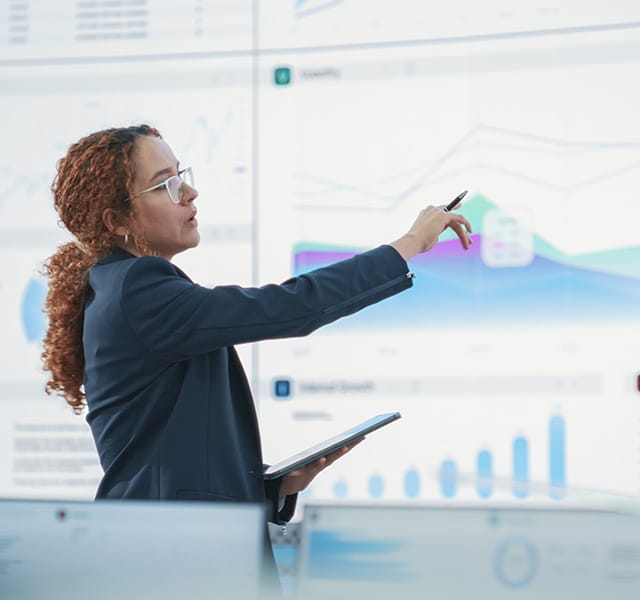A woman is standing at a digital board, pointing at a data graph