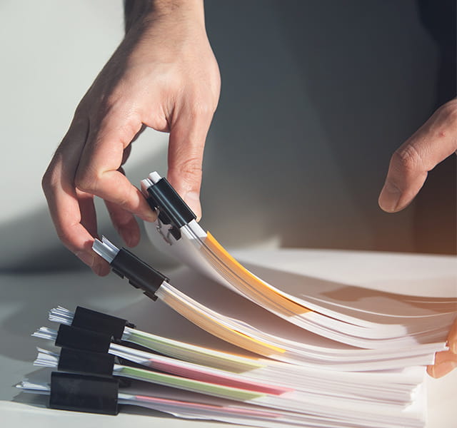 A close up of someone piling up a page of paper reports. Each report is held together by a bulldog clip