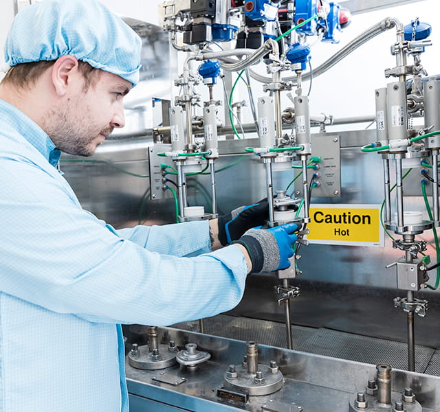 A man wearing a hair covering, overalls and gloves is inspecting equipment