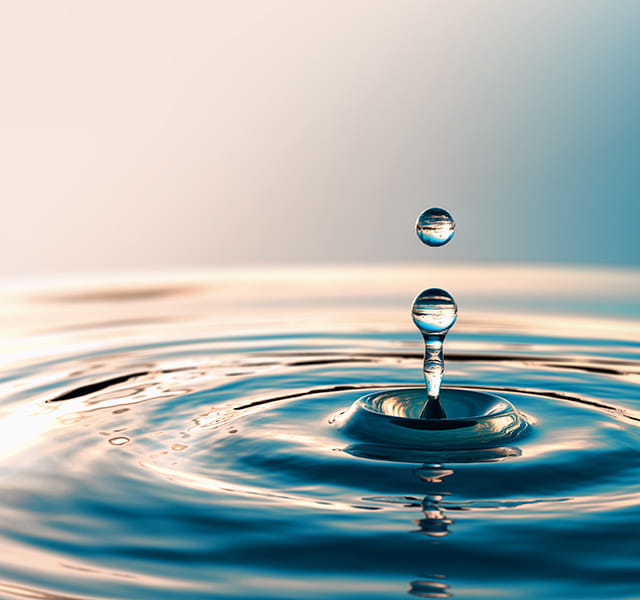 A drop of water rippling in a plain cream to sky blue gradient background