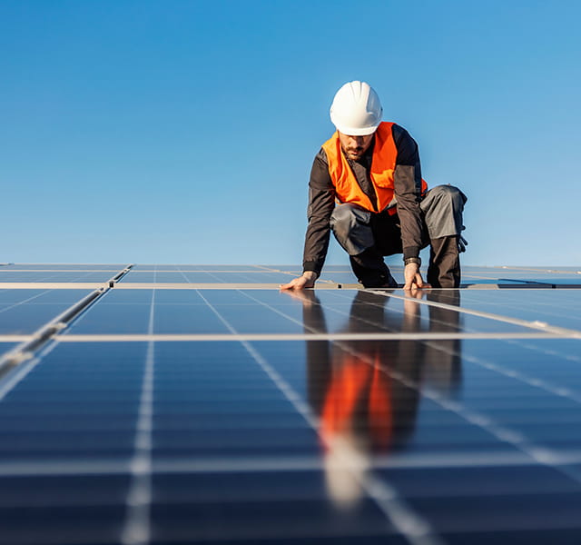 A man in a hi-vis and hard hat is pressing his hands onto a solar panel on a flat surface