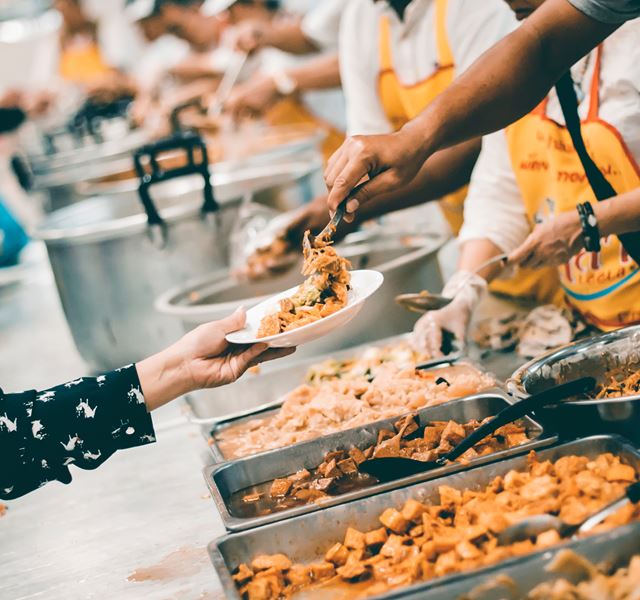 Food is being served from large warmers onto a person with a plate in their outstretched hand