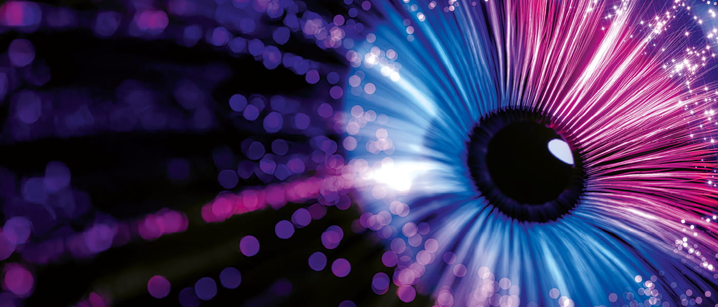 A dark background with flashes of blue, pink and purple. To the right of the image is the iris and pupil of a human eye, the iris is a mixture of the purple, pink and blues from the flashes shown in the rest of the image