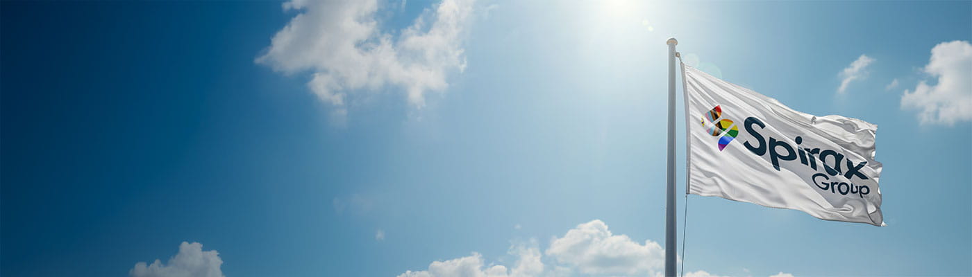a white flag with the Spirax Group logo on it in the colours of the Pride rainbow in the S flies amongst a light blue sky with light fluffy clouds