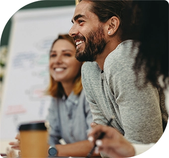 A close up of three people sitting around a larger table, two women and a man. One is holding a takeaway cup of coffee. 