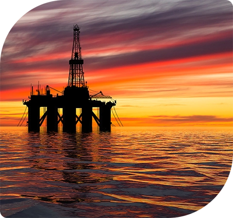 An oil platform in the middle of the sea at sunset. The sunset is pink and orange with dark grey clouds. 
