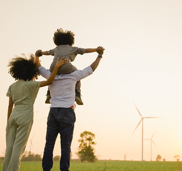 An adult outside playing with two children, there is a wind turbine in the far distance. 