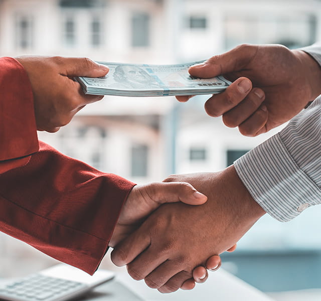 Two people shaking hands while exchanging money