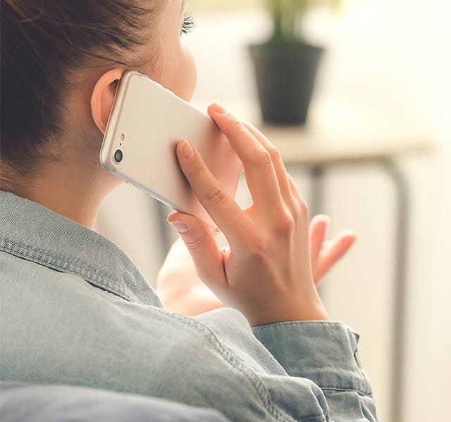 A woman making a phone call on a mobile phone, her back is to the camera, her face obscured by the phone